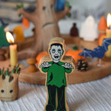 A Lanka Kade green and black Frankenstein style monster wooden figure placed in front of a Halloween themed Grimm's celebration ring set up. 