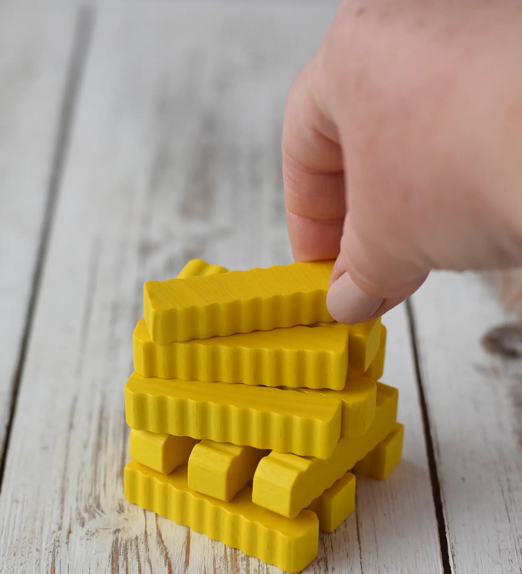 Erzi wooden play food crinkle cut chips placed on a wooden surface. An adult's hand is picking up one of the chips from a stack.