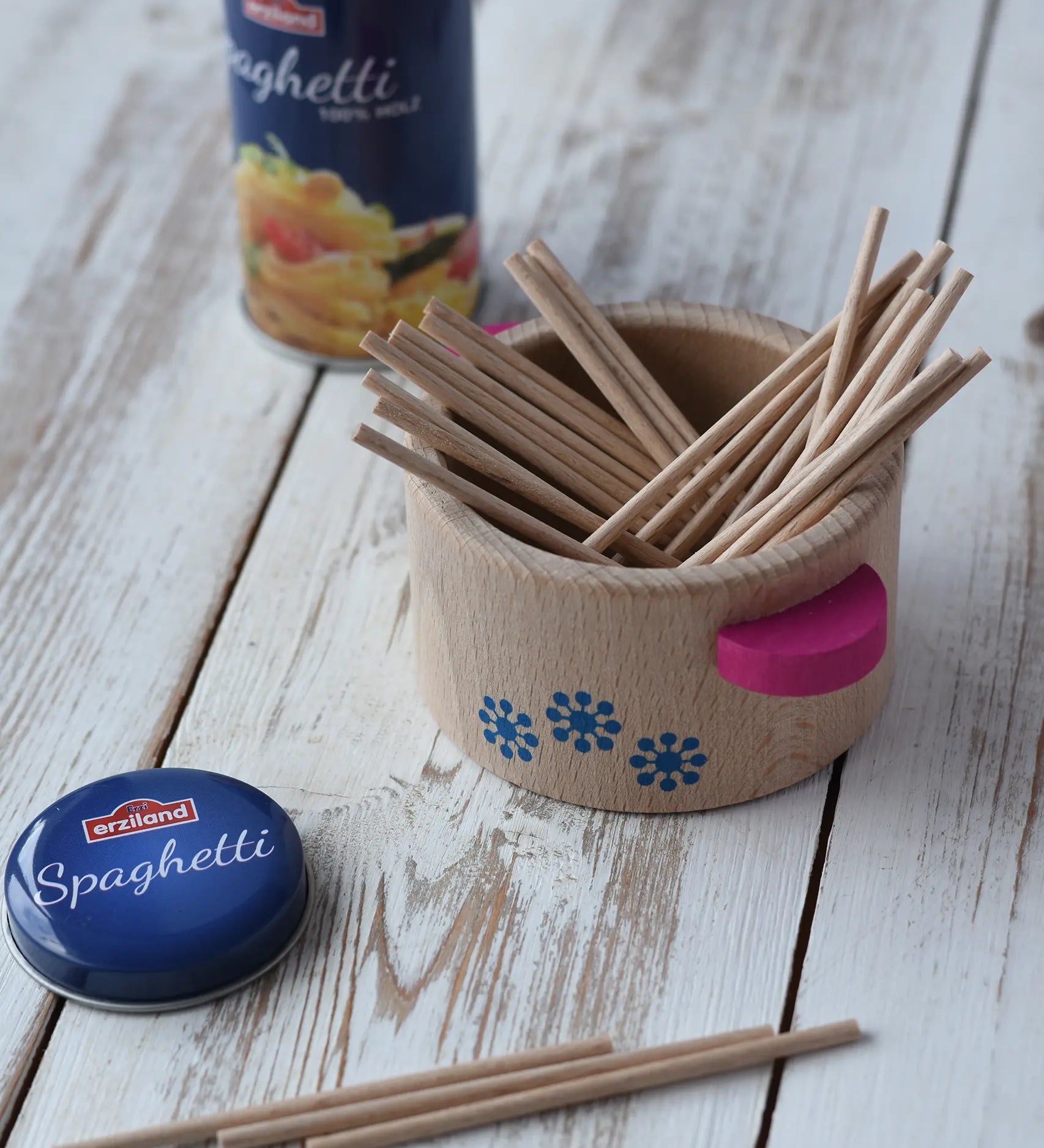 Erzi spaghetti strands placed in a wooden cooking pot with the blue tin in the background.