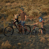 A parents with children taking a bike ride through a grassy area. A child behind the parent is riding the Early Rider Seeker X16 16" Bike - Brushed Aluminium