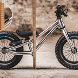 The Early Rider Big Foot Balance Bike stood in front of a light brown wooden ruler, showing the height from the floor to the top of the black seat