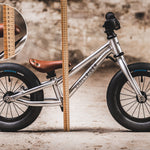 The Early Rider Charger Balance Bike stood behind a light brown measuring ruler, showing the height from the floor to the top of the bike seat