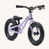 The Early Rider Big Foot Balance Bike - Violet Haze is stood at a slight angle. It has a Violet frame, black wheels, a black seat and black handle bars. The image is on a cream background