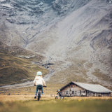 Two Children on Early Rider 'Seeker' bikes in a mountainous landscape with a wooden cabin in the background.
