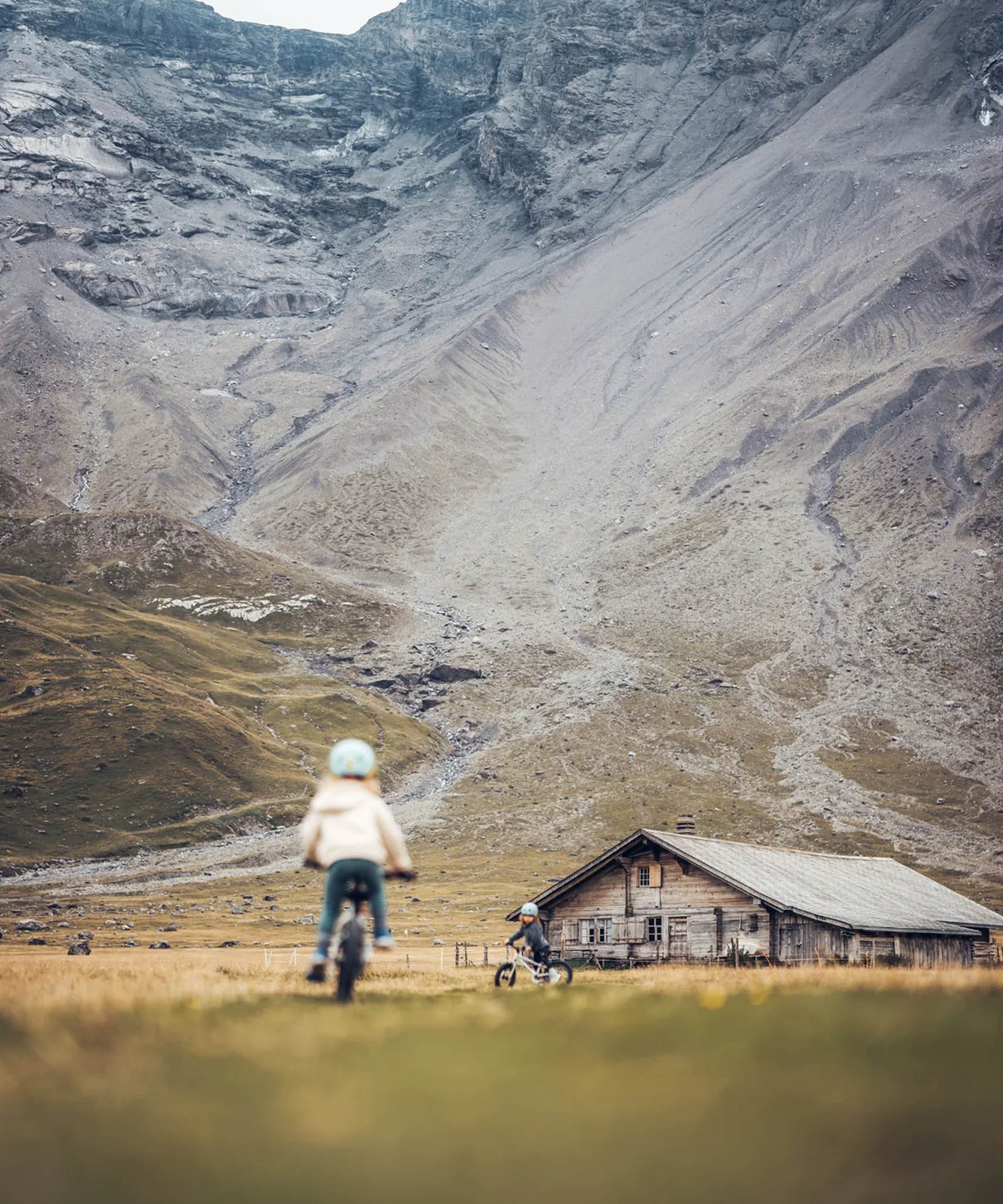 Two Children on Early Rider 'Seeker' bikes in a mountainous landscape with a wooden cabin in the background.
