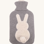 The Ecoliving Natural Rubber Hot Water Bottle - Bunny, has a soft grey knitted cotton cover with a fluffy white bunny silhouette and a cute white cotton tail. The image is on a cream background