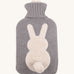 The Ecoliving Natural Rubber Hot Water Bottle - Bunny, has a soft grey knitted cotton cover with a fluffy white bunny silhouette and a cute white cotton tail. The image is on a cream background