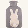 The Ecoliving Natural Rubber Hot Water Bottle - Bunny, has a soft grey knitted cotton cover with a fluffy white bunny silhouette and a cute white cotton tail. The image is on a cream background