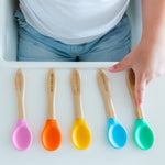 5 bamboo baby weaning spoons lined up on a high chair with a toddler choosing the colour they would like. 