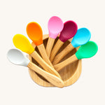 7 bamboo baby spoons with colourful silicone heads in a bamboo feeding bowl. 