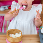 Toddler wearing a white dress eating icecream at a wooden table from the Eco Rascals Bamboo Bowl & Spoon Weaning Set in pink silicone.