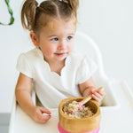Toddler in a highchair eating porridge from the Eco Rascals Bamboo Bowl & Spoon Weaning Set in pink silicone.