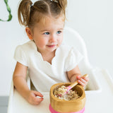 Toddler in a highchair eating porridge from the Eco Rascals Bamboo Bowl & Spoon Weaning Set in pink silicone.