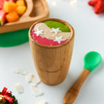 A colourful smoothie in pink, cream and green in a bamboo baby cup with green silicone and bamboo baby spoon. 