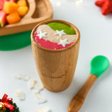 A colourful smoothie in pink, cream and green in a bamboo baby cup with green silicone and bamboo baby spoon. 