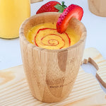 A yellow mango smoothie with red strawberry puree swirl in a bamboo baby cup, decorated with strawberry slices..
