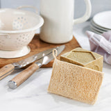 A close up of the Ecoliving loofah kitchen sponge scrubber available at Babipur showing the loofah side of the sponge proped up against a Ecoliving dish soap with other utensils in the background