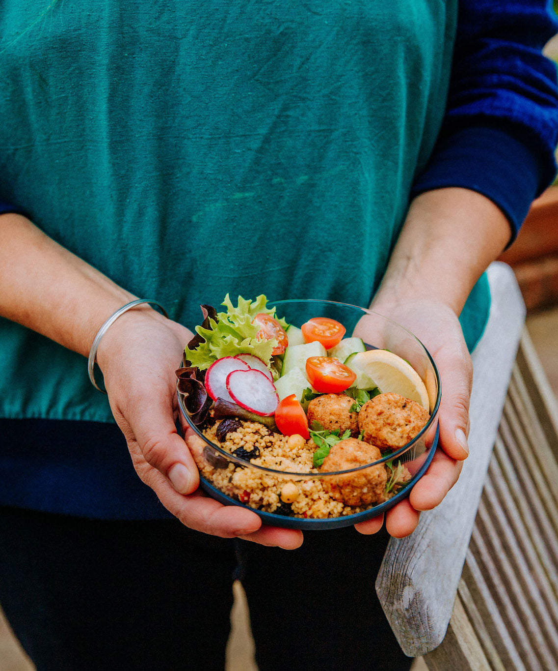 An adult hand holding the medium Elephant Box medium lunch bowl with the lid off and full of food. 