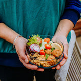 An adult hand holding the medium Elephant Box medium lunch bowl with the lid off and full of food. 