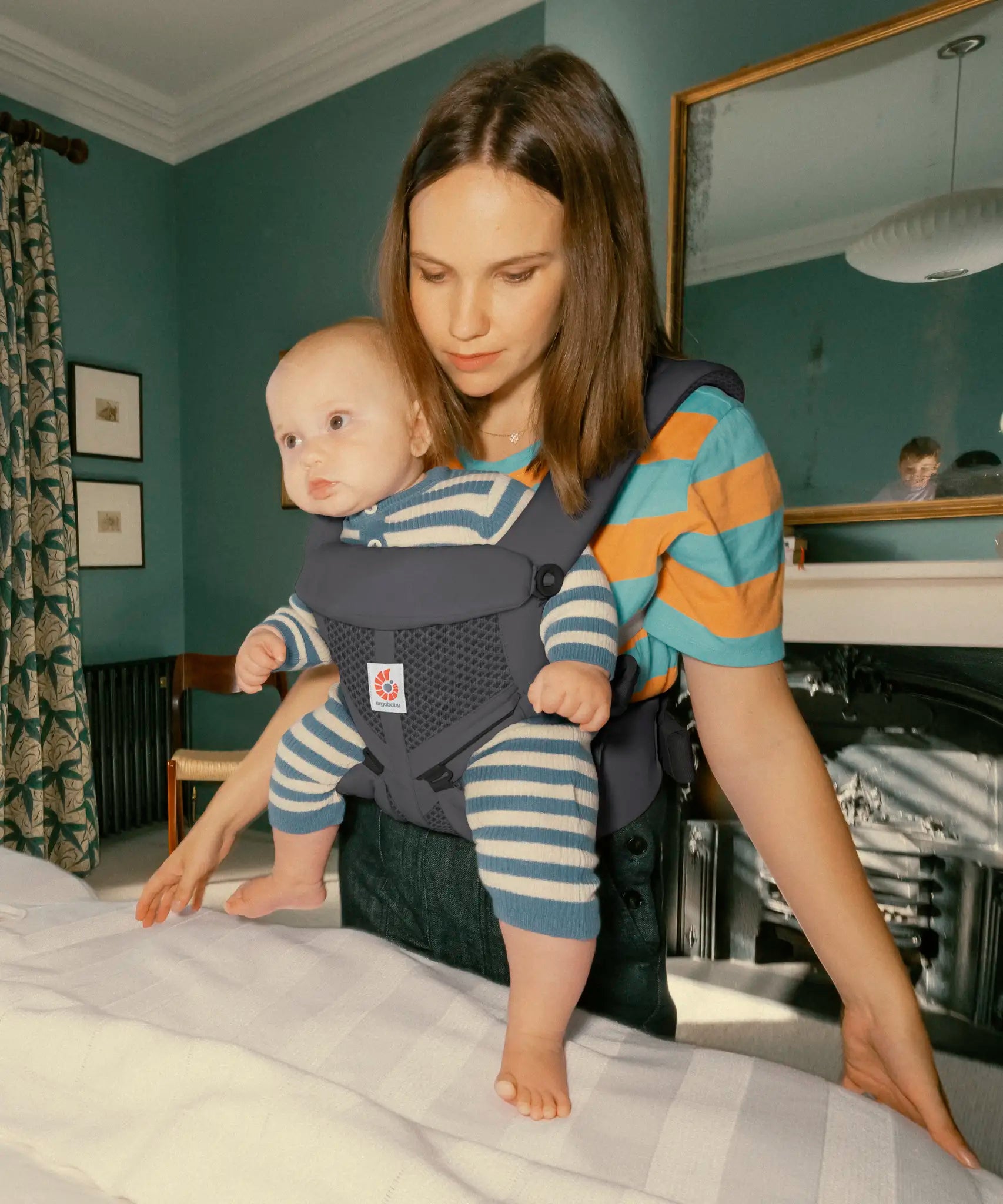 Mother carrying baby in the Ergobaby charcoal grey omni 360 air mesh carrier in the bedroom 