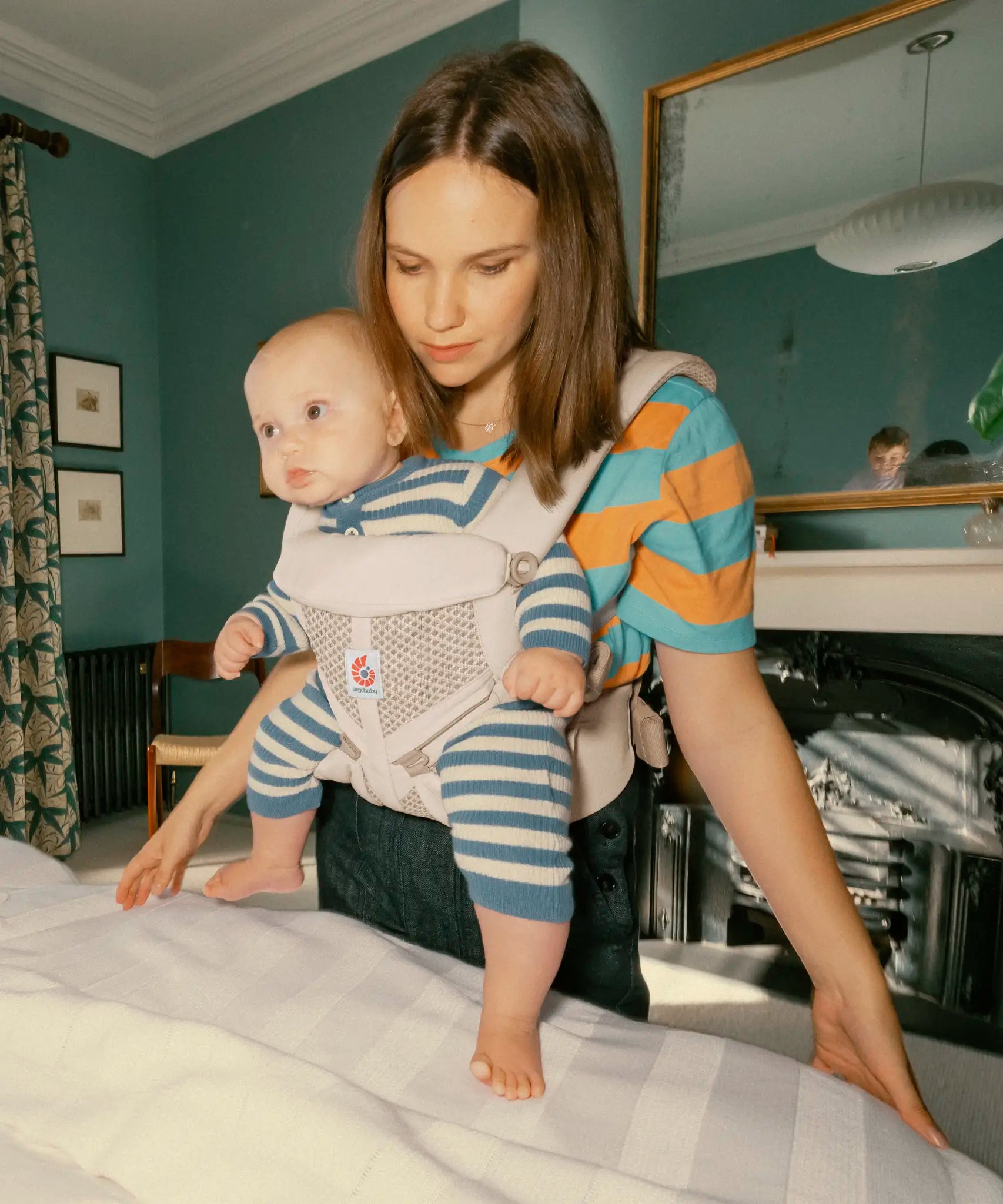 Mother carrying baby in the Ergobaby natural beige omni 360 air mesh carrier in the bedroom 