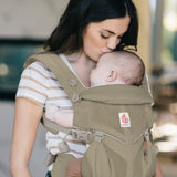 Mother carrying baby in a soft olive green Ergobaby omni 360 cool air mesh baby carrier and kissing baby's head