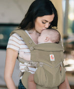 Mother carrying baby in a soft olive green Ergobaby omni 360 cool air mesh baby carrier and kissing baby's head