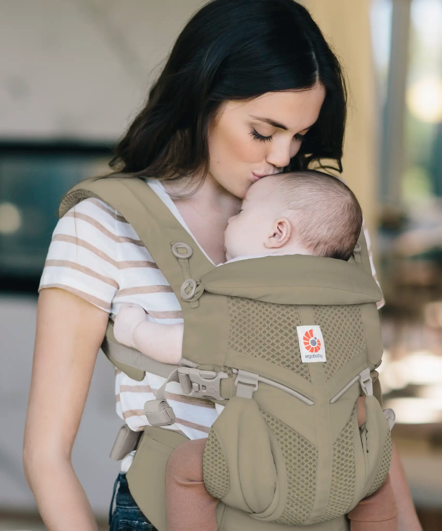Mother carrying baby in a soft olive green Ergobaby omni 360 cool air mesh baby carrier and kissing baby's head