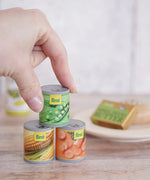 Erzi Tinned Vegetables (carrots, peas, sweetcorn), wooden canned veggie play food, stacked in a play set up with a hand for scale.