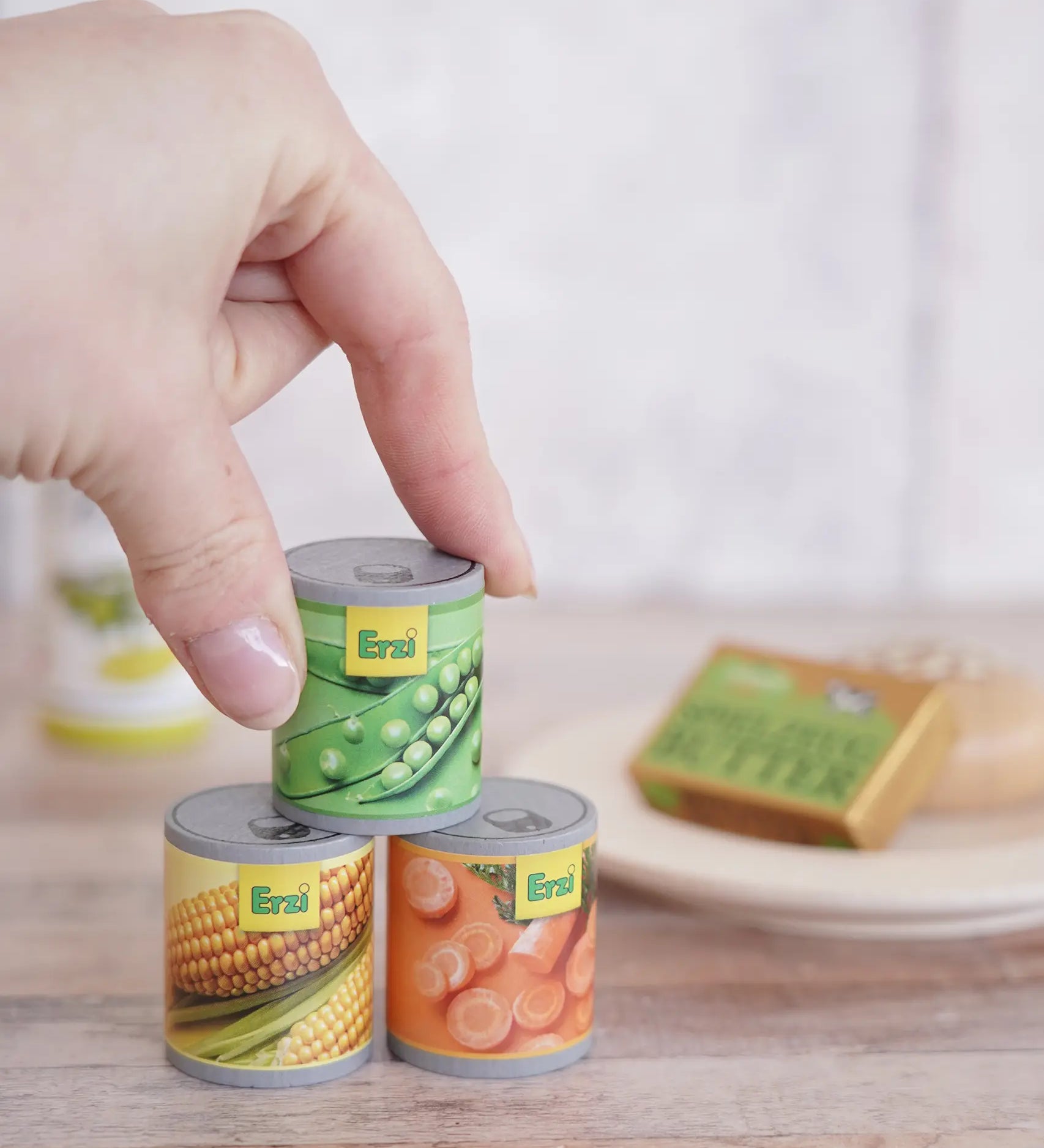 Erzi Tinned Vegetables (carrots, peas, sweetcorn), wooden canned veggie play food, stacked in a play set up with a hand for scale.