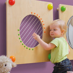 A child happily plucking the strings on the Erzi Baby Guitar Wall Board. Perfect for little musical maestros 