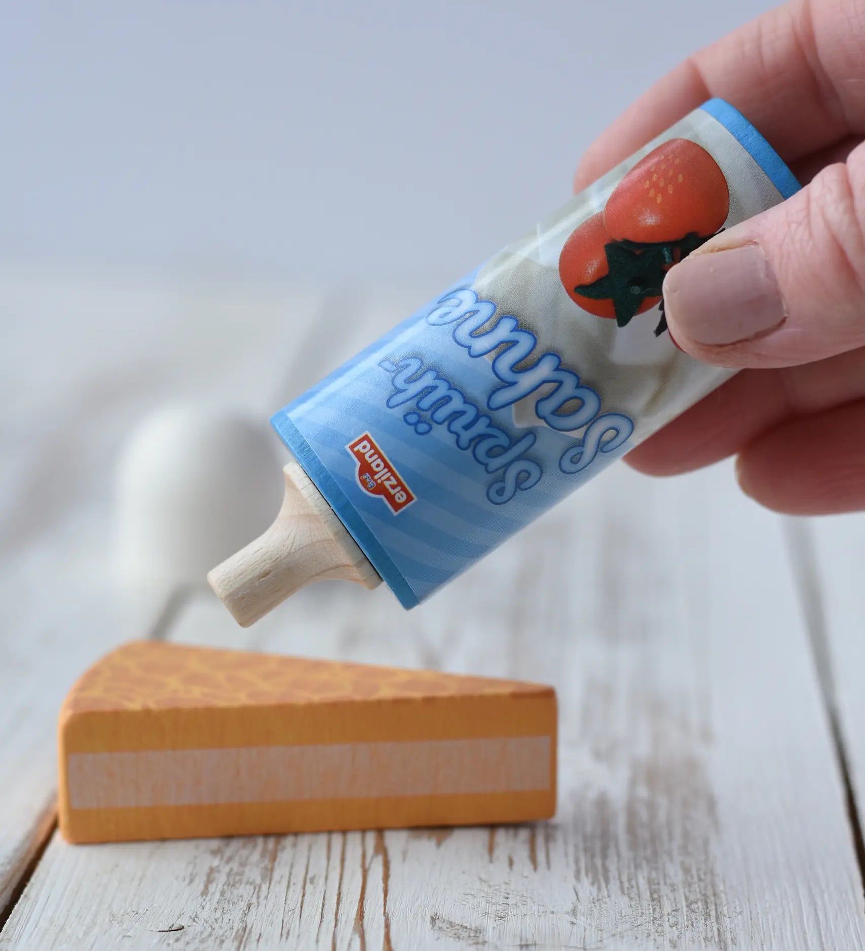 Erzi Toys Whipped squirty Cream wooden play food with the lid taken off in an adult's hand hovering over a cake.