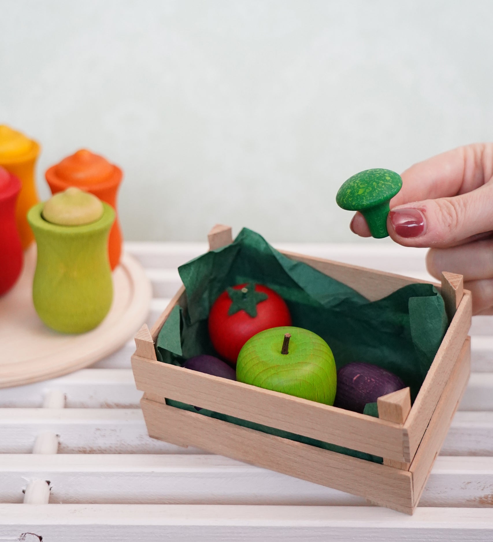 A hand holding a small wooden broccoli toy by Erzi, perfect for a play kitchen, sold at Babipur.
