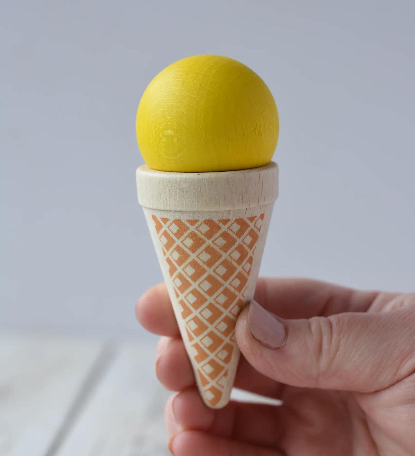 Erzi yellow vanilla ice cream cone wooden play food in an adult's hand.