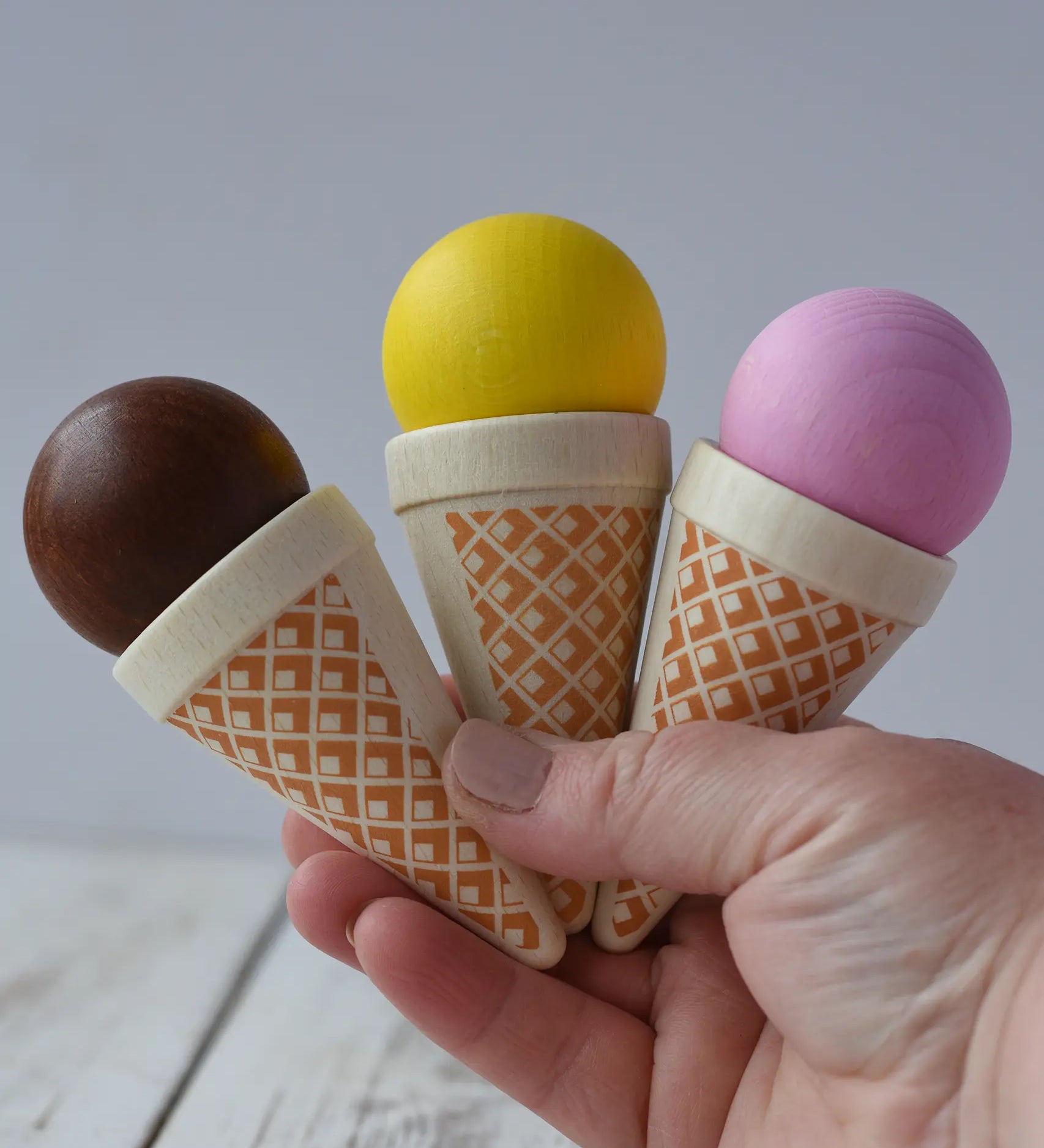 Three Erzi ice cream cones wooden play food in an adult's hand.