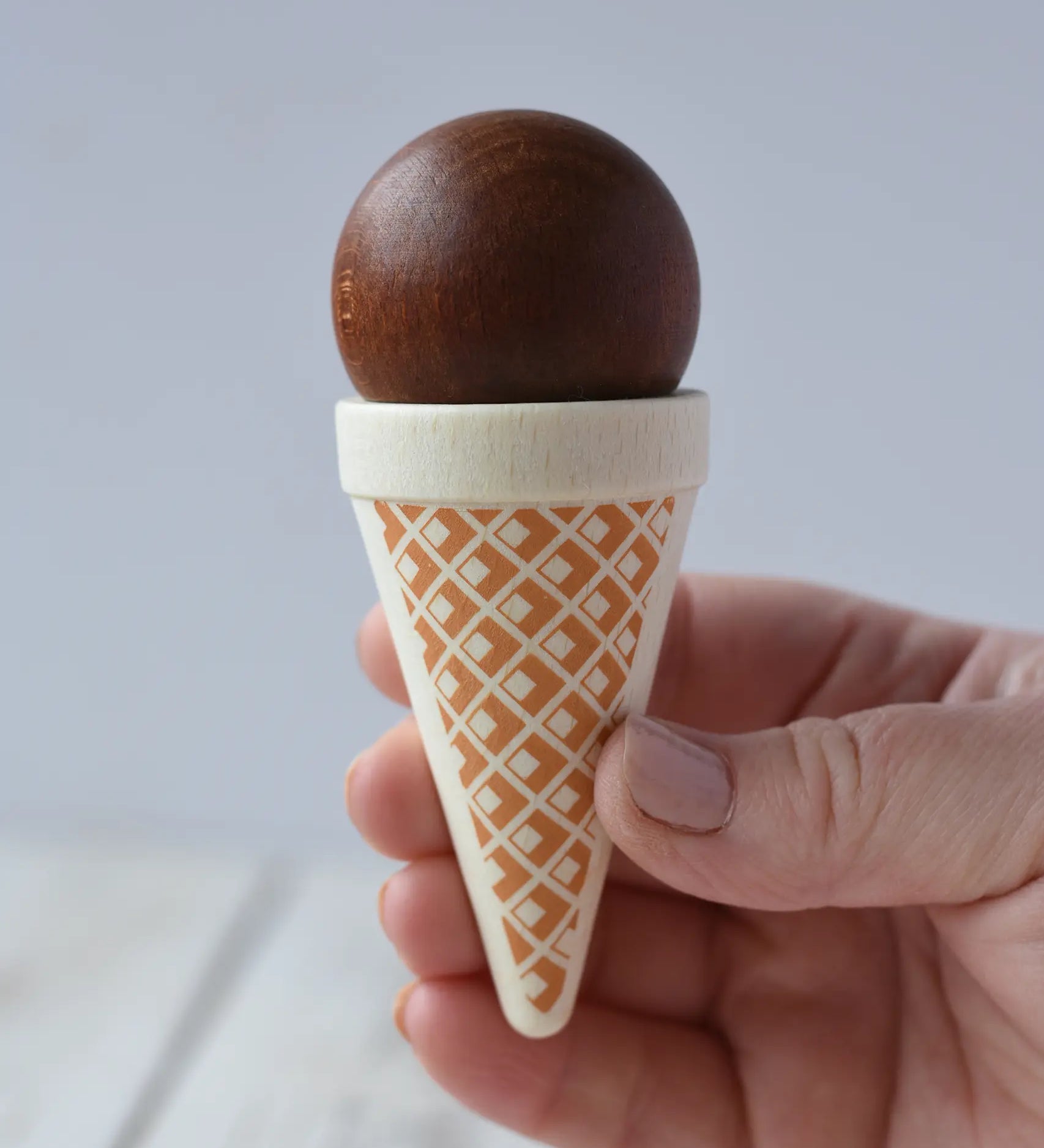 Erzi brown chocolate ice cream cone wooden toy play food in an adult's hand. 