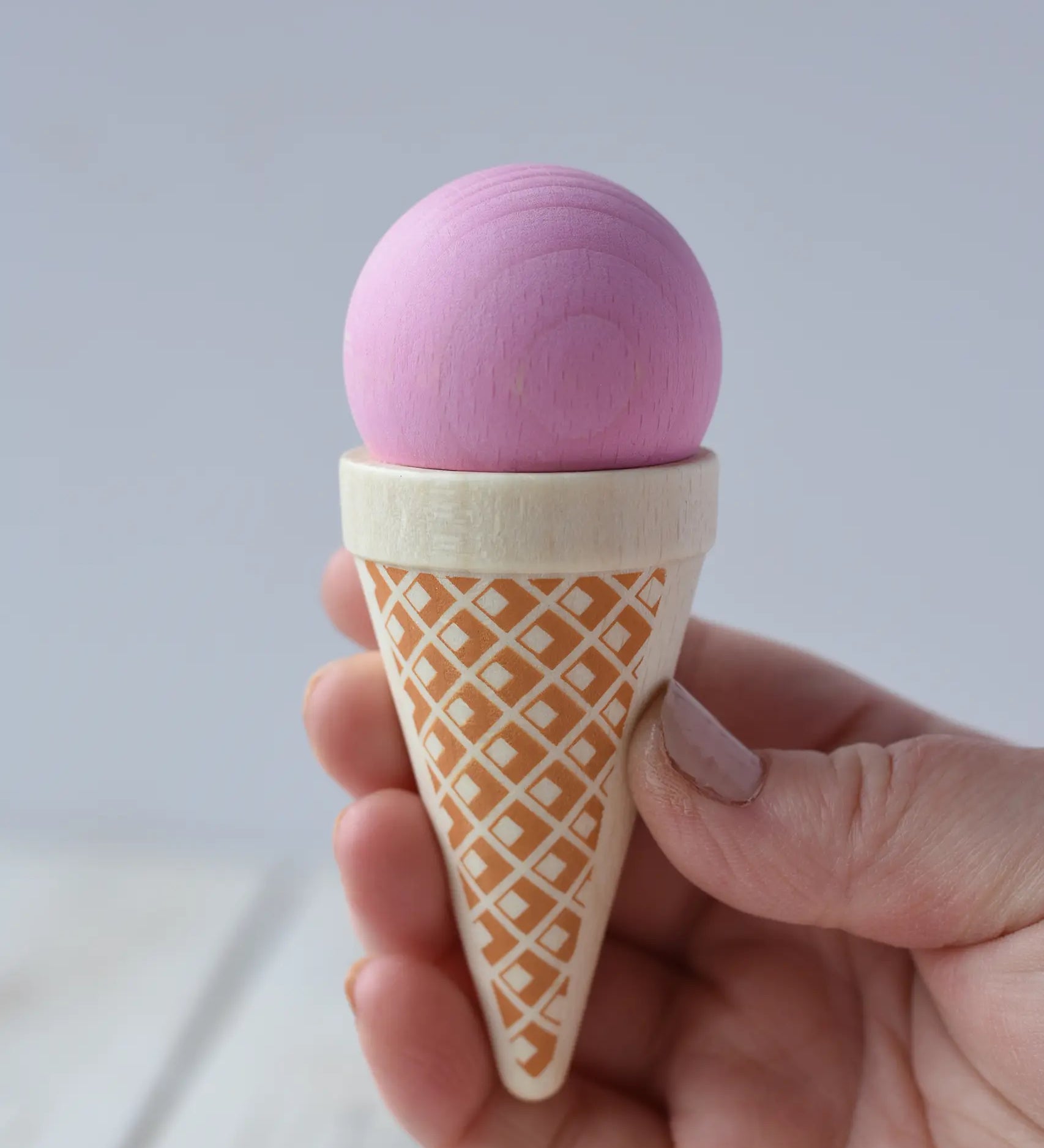 Erzi pink strawberry ice cream cone wooden play food in an adult's hand.