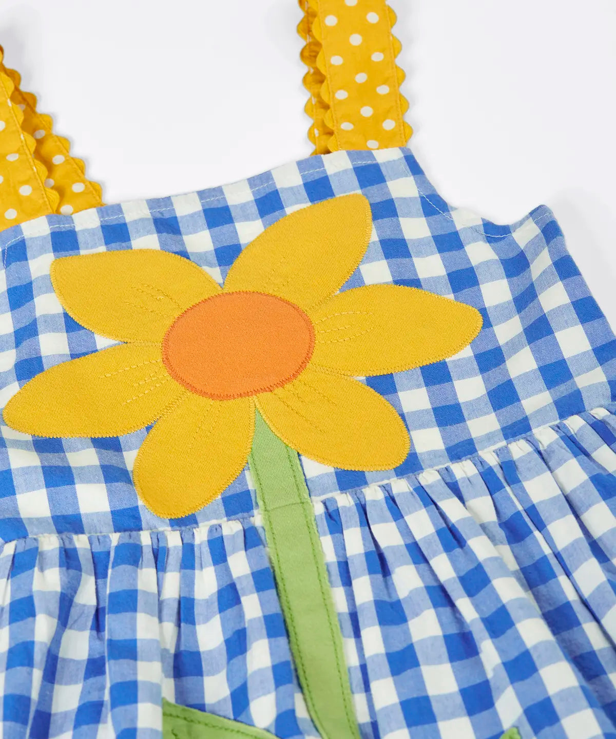 Frugi 100% organic cotton dress in blue and white gingham laid flat showing  a large sunflower patch and yellow shoulder straps