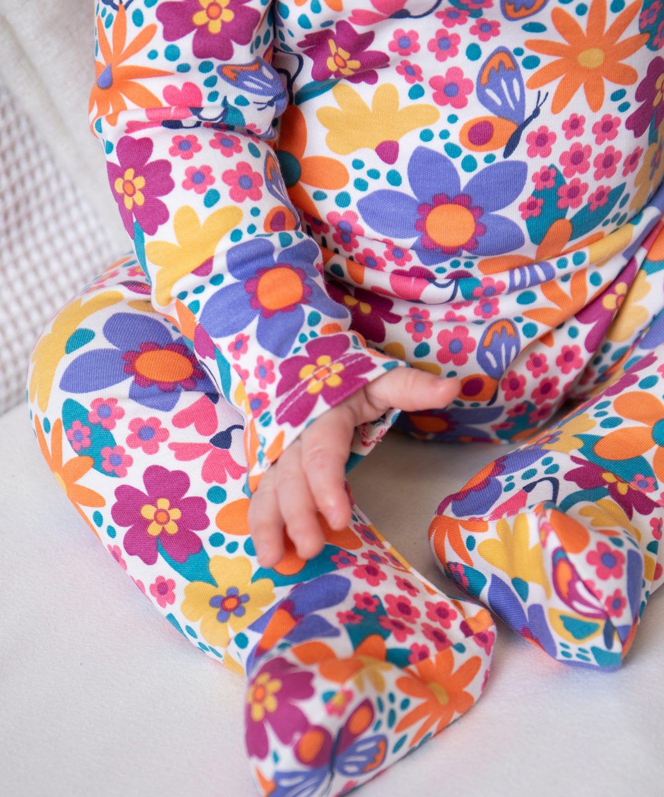 A close up of a baby wearing the GOTS organic cotton Frugi easy dressing printed baby in white/retro floral design available at Babipur.