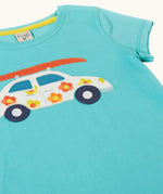 Frugi 100% organic cotton short sleeve t-shirt in light blue laid flat showing  white car patch carrying a surfboard on the front