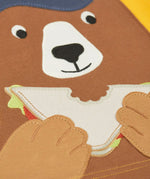 Close up of the playful brown bear eating a sandwich patch on the Frugi 100% organic cotton yellow short sleeve t-shirt