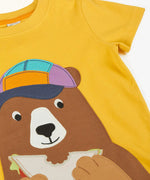 Frugi 100% organic cotton yellow short sleeve t-shirt laid flat showing a playful brown bear eating a sandwich patch on the front