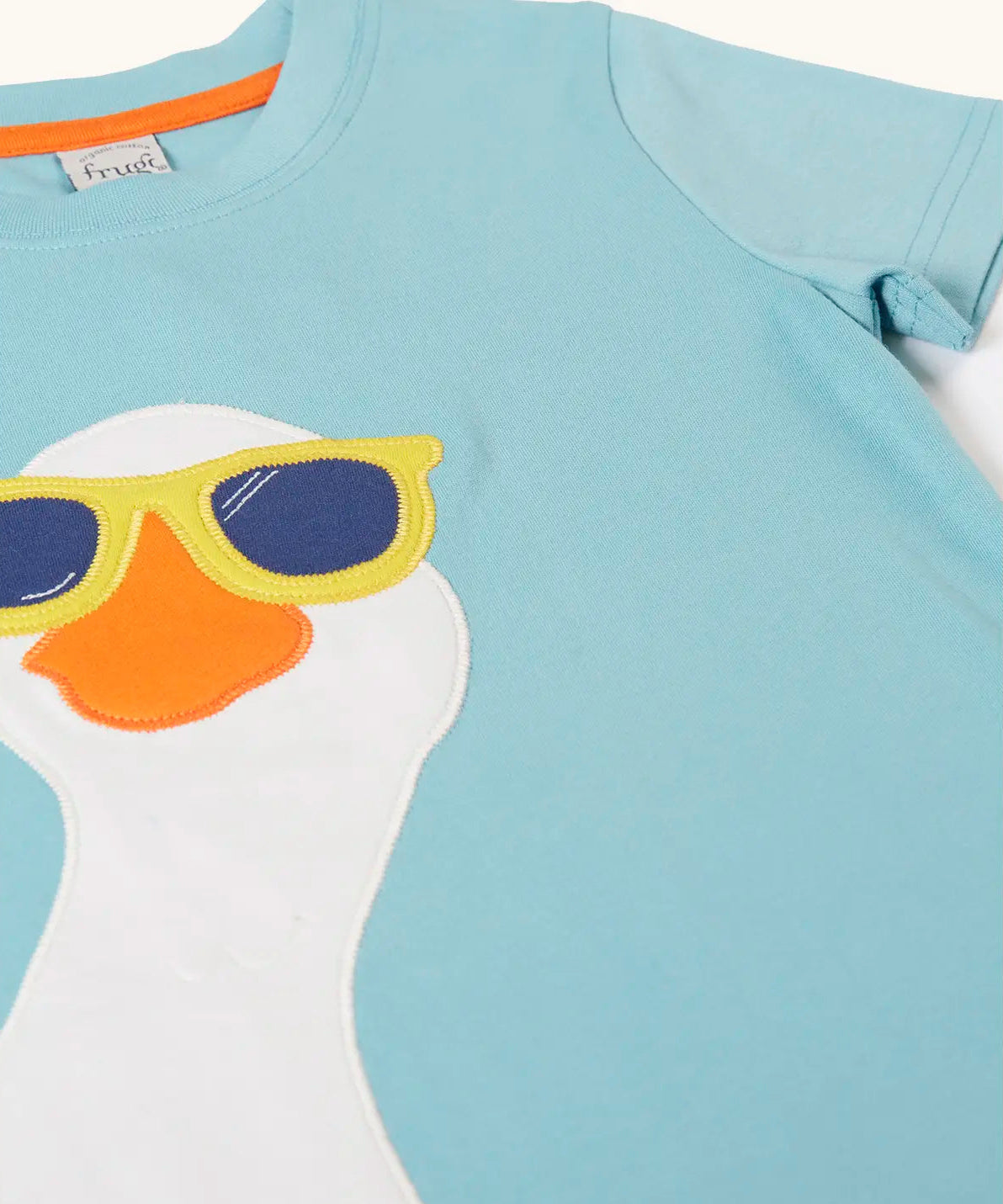 Frugi 100% organic cotton short sleeve t-shirt in light blue laid flat showing  a playful white goose wearing sunglasses patch on the front