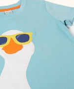 Frugi 100% organic cotton short sleeve t-shirt in light blue laid flat showing  a playful white goose wearing sunglasses patch on the front