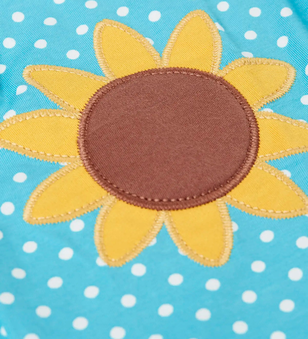 Close up of Frugi 100% organic cotton Dora playsuit in blue with white dots showing sunflower patch detail