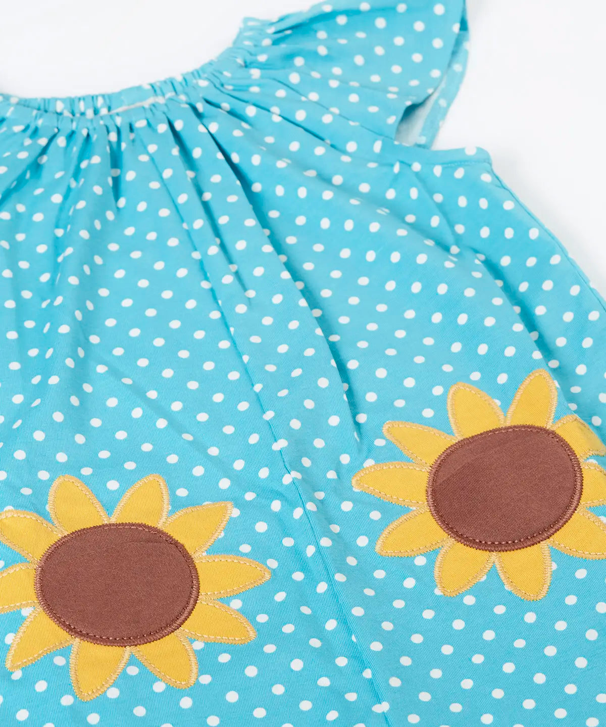 Frugi 100% organic cotton Dora playsuit in blue with white dots laid flat showing the sunflower patches on the front and elasticated neck line