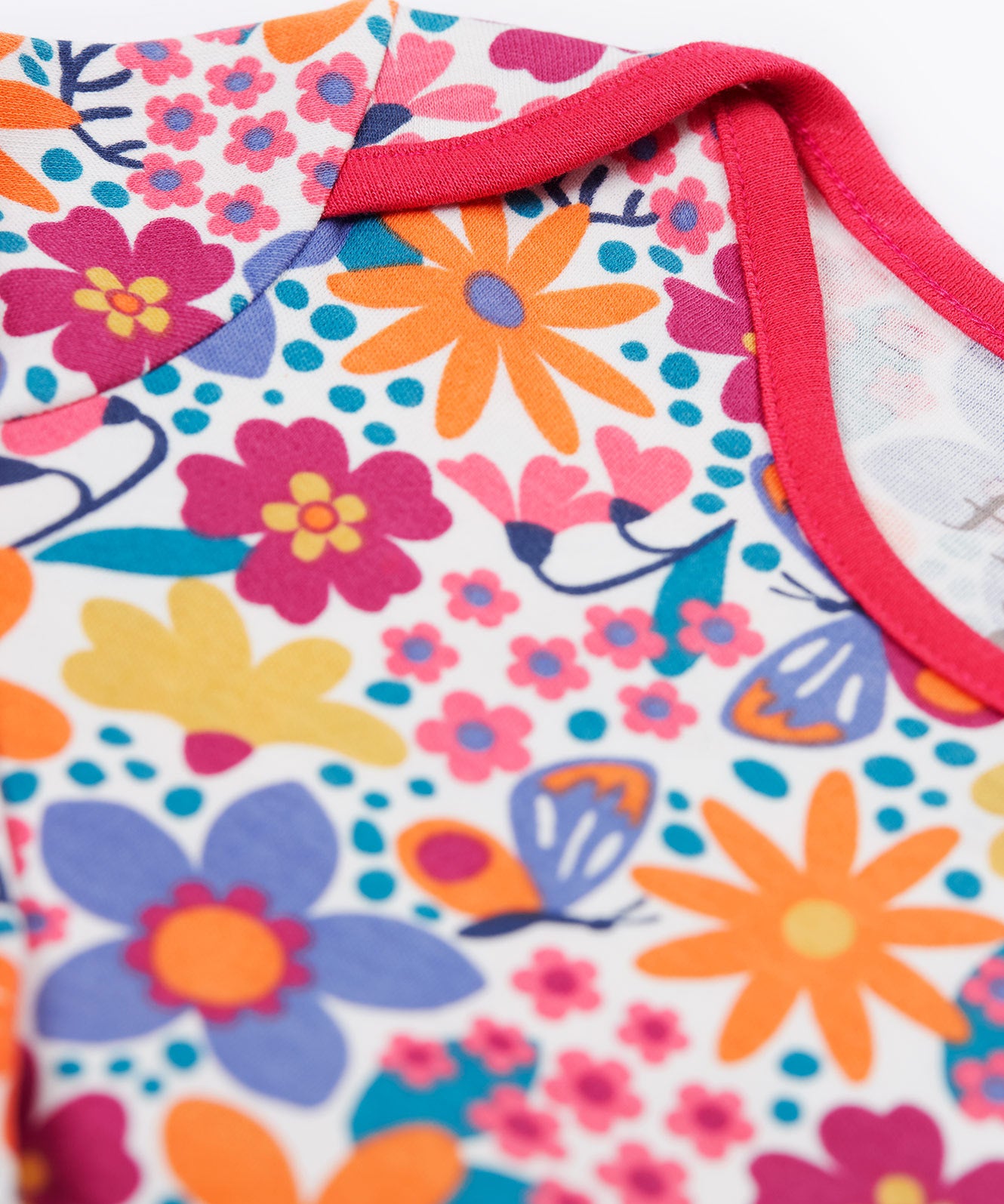 A close up of the pink trim detail on the neck and shoulder on the Frugi easy dressing printed babygrow in white/retro floral design available at Babipur.