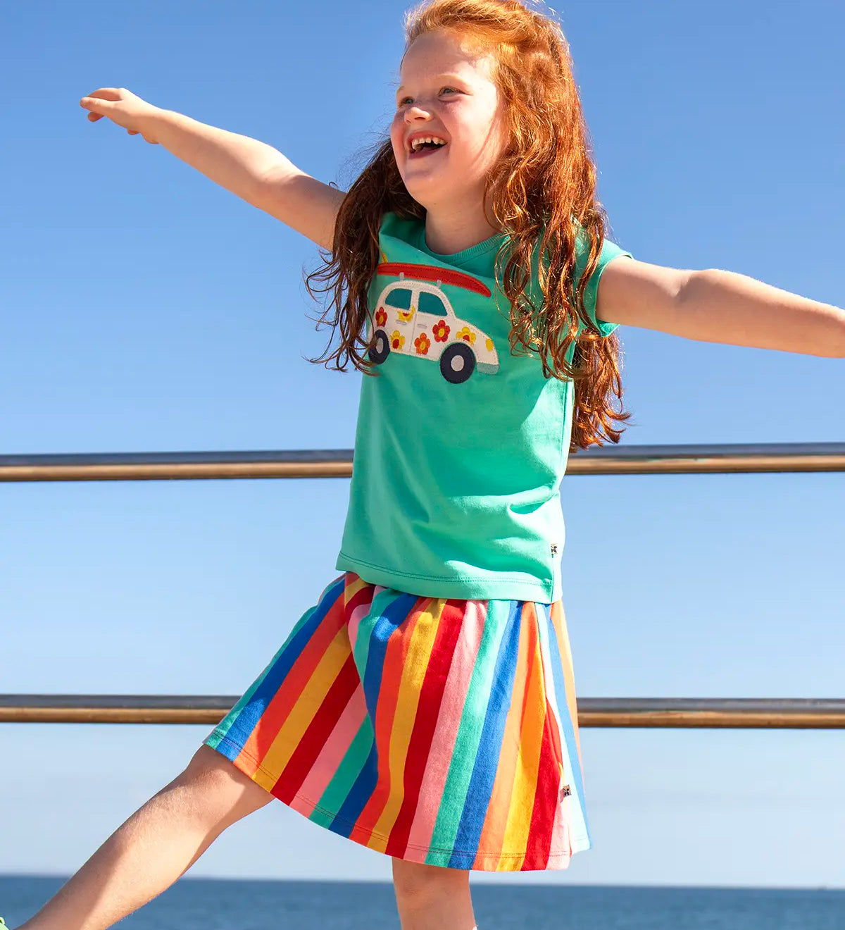 Child wearing Frugi Alba skort in rainbow stripes with the ocean in the background