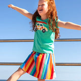 Child wearing Frugi Alba skort in rainbow stripes with the ocean in the background