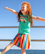 Child wearing Frugi Alba skort in rainbow stripes with the ocean in the background